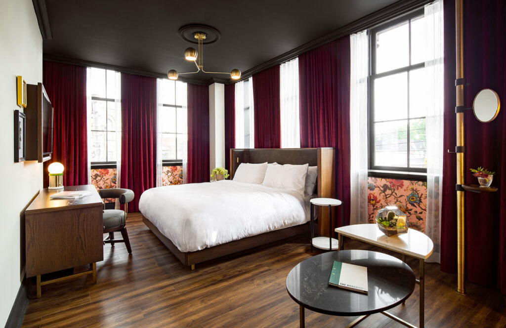 Bedroom at the Broadview Hotel with maroon curtains and lush white bedding.