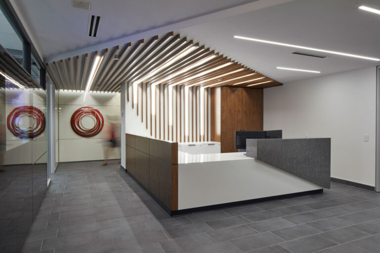 Reception area with gray tile flooring, and sculptural reception desk with wood and marble accents.