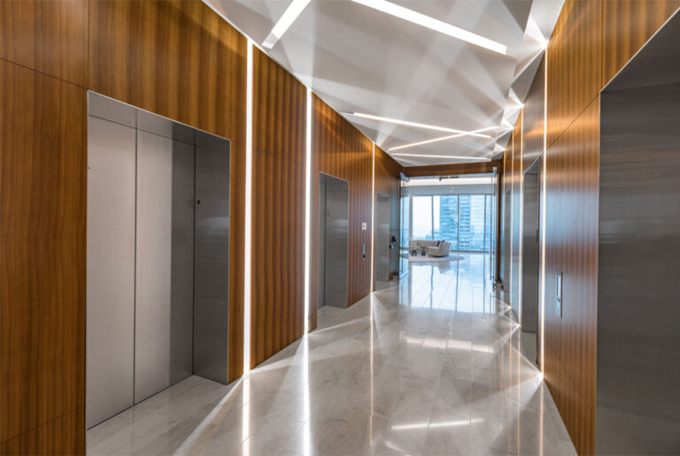Elevator bank with wood panelled walls and diagonal lighting accents along the ceiling.
