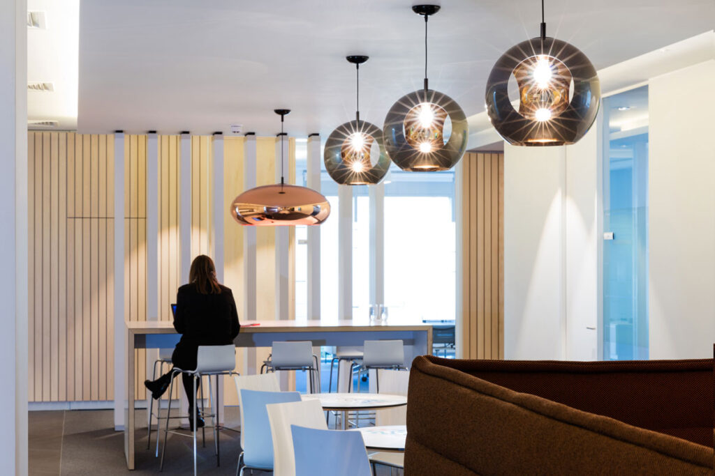 Employee breakout space with white tables and high top counter with modern lamps hung overhead.