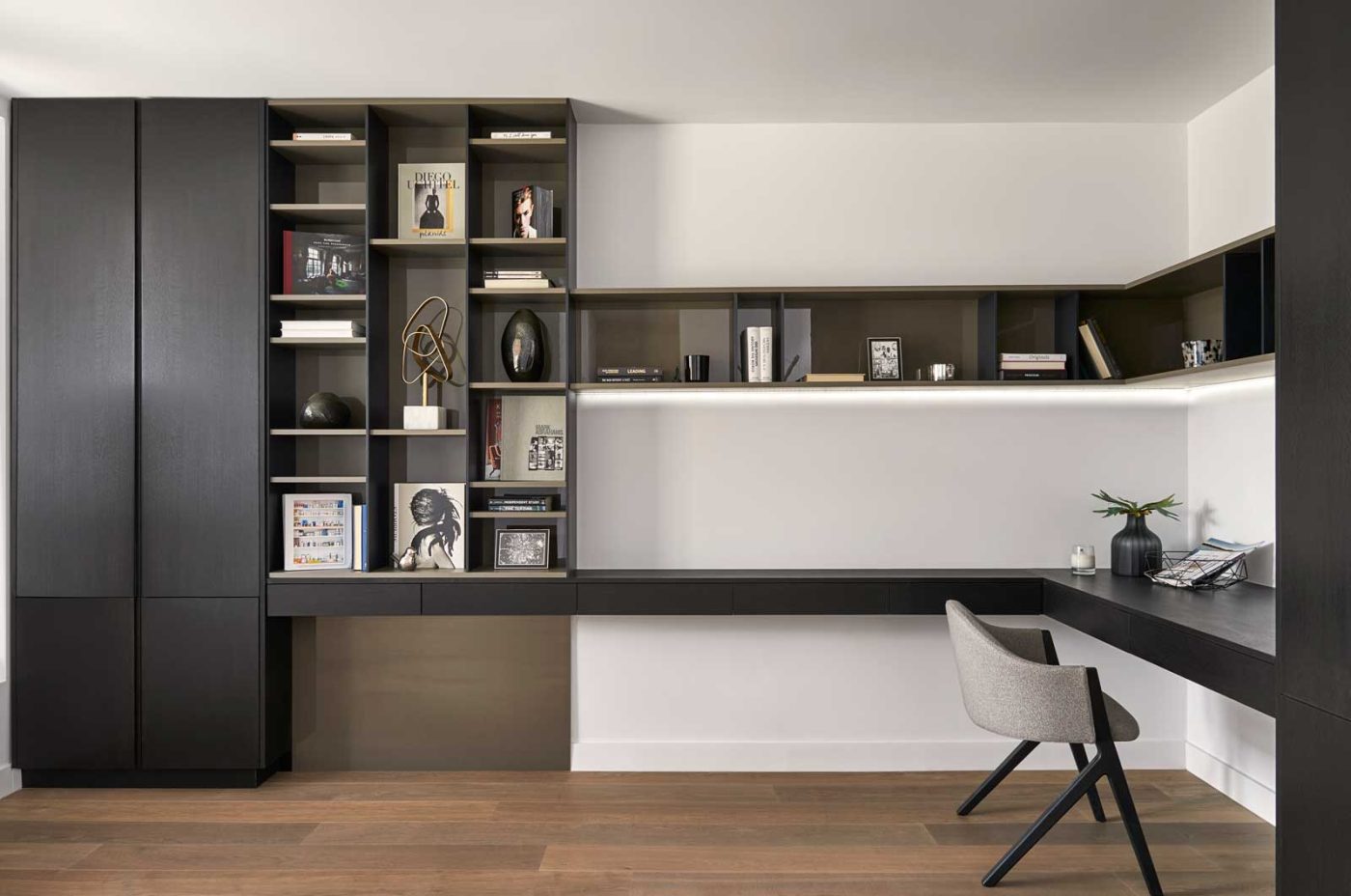 A set of black shelves with nooks abutts a long floatingdesk with a shelf above.