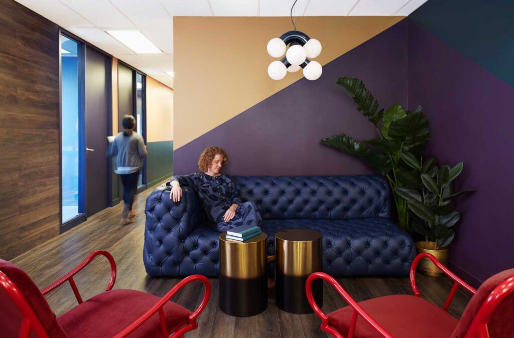 A tufted blue leather couch against a wall with graphi accents is the welcome to this office space.