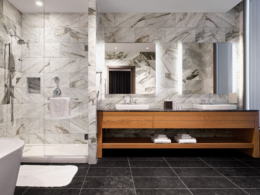 Hotel bathroom with two sinks, gray stone walls and a shower lined with gray stone.