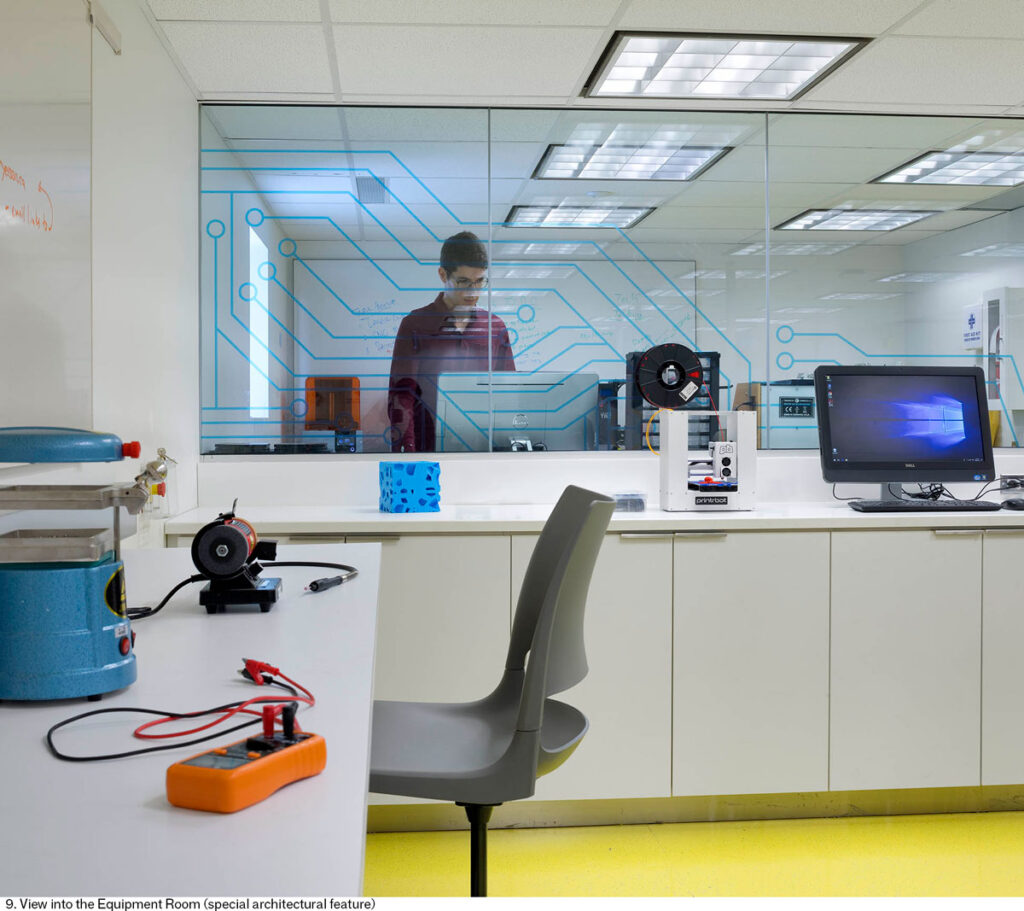 A student works in a lab behind a window where a film patterned with computer circuits has been applied.