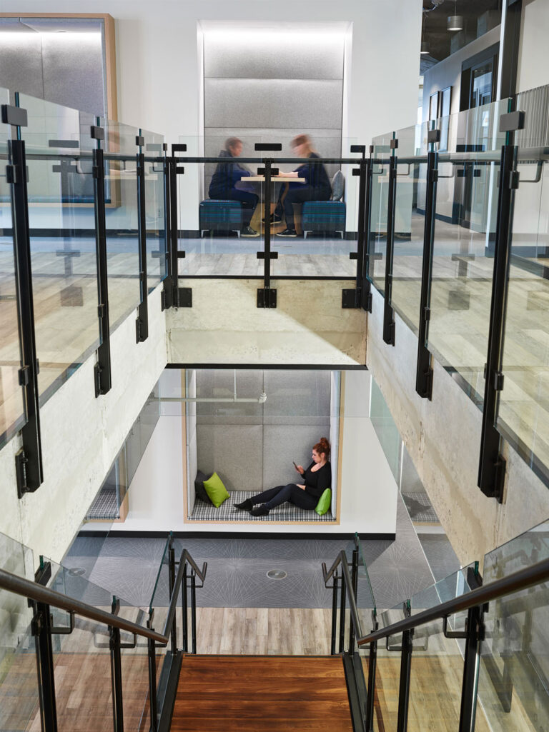 View down a set of connecting stairs with glass partitions and black metal supports.