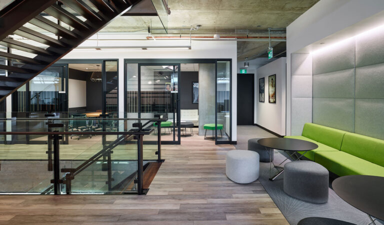 Open lounges surround the stair, with green and gray seating and adjacent glasswalled meeting rooms.