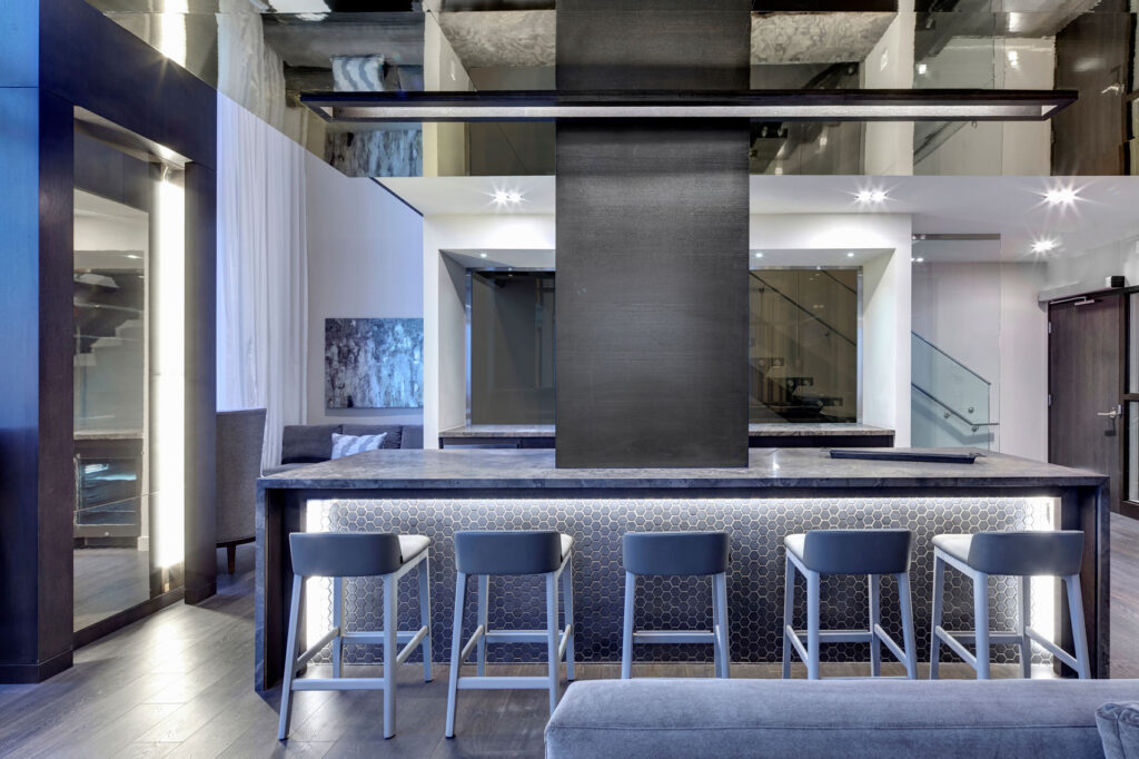 Kitchen amenity space with waterfall marble counter, pale gray bar stools and reflective ceiling.