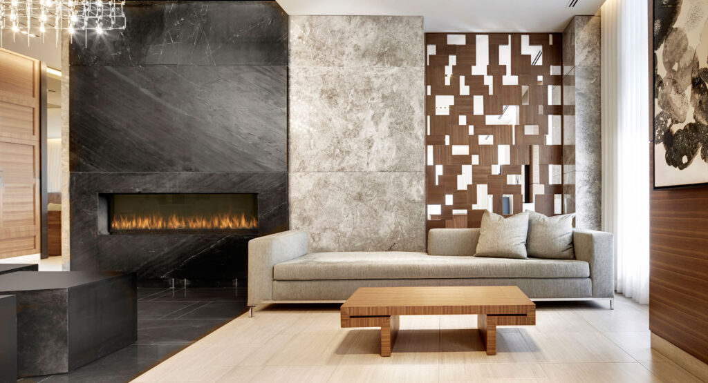 A condo lobby with long pale couch, next to a fireplace surrounded by black stone.