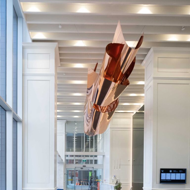 The undulating layers of the copper sculpture shine against the ridged ceiling.