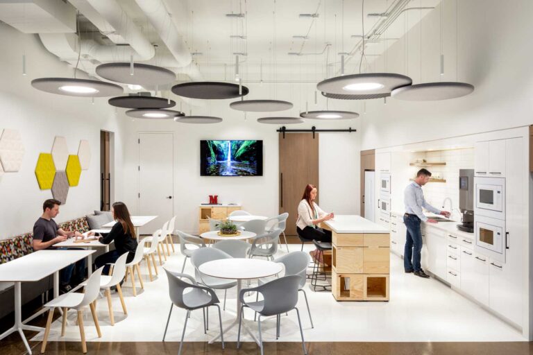 An employee kitchen space is a clean white break with marble topped island and four top tables.