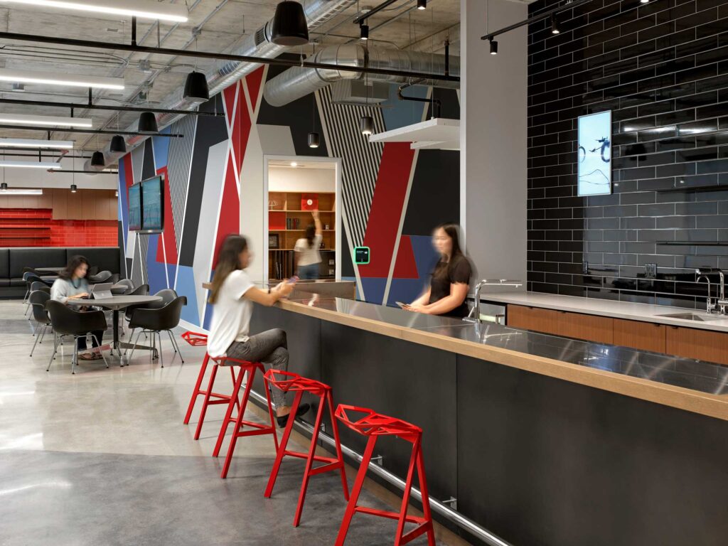 Employees gather in the cafe space with black tiled walls and a geometric mural in red, blue and black.
