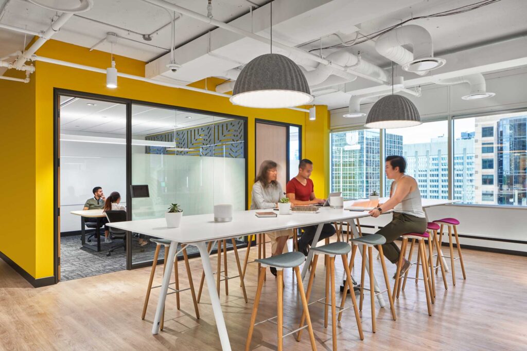 Staff meet at a high top table at Uber's Toronto office next to a glass walled meeting room with decorative wall.
