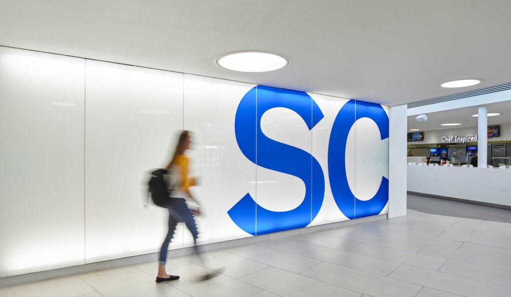 A student walks by a brand graphic of a cobalt blue SC on a white wall.