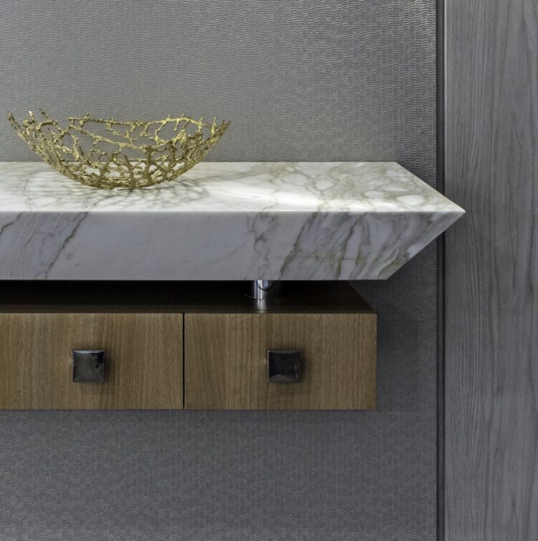 Close-up image of a modern custom designed catch-all cabinet with a marble top and blonde wood covered drawers for storage underneath, with decorative chrome pulls.