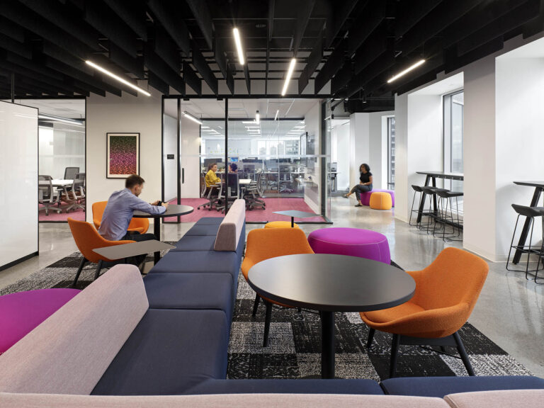 A communal work/lounge area with desks and colorful benches in the foreground and offices and meeting rooms in the background