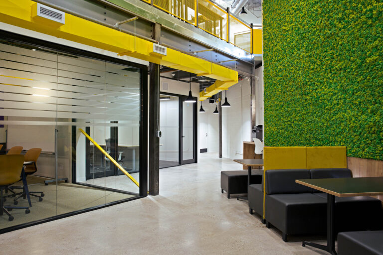 Living wall and communal seating are on the right side and offices behind glass walls on the left