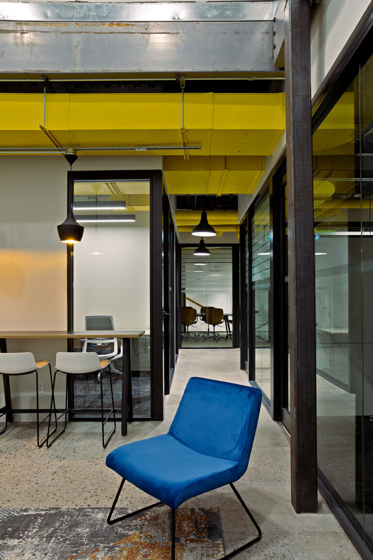 Blue chair in the communal area of the co-working space, offices behind glass walls showing in the background