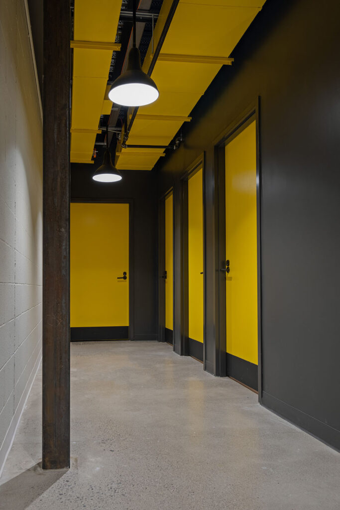 Hallway space with dark walls and bright yellow doors and yellow accents along the ceiling
