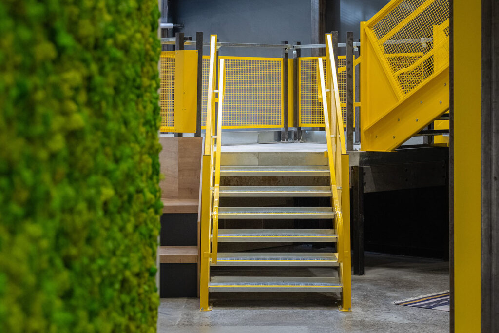 Close up of the yellow staircase to the second floor with the living wall edge peeking through on the left side.