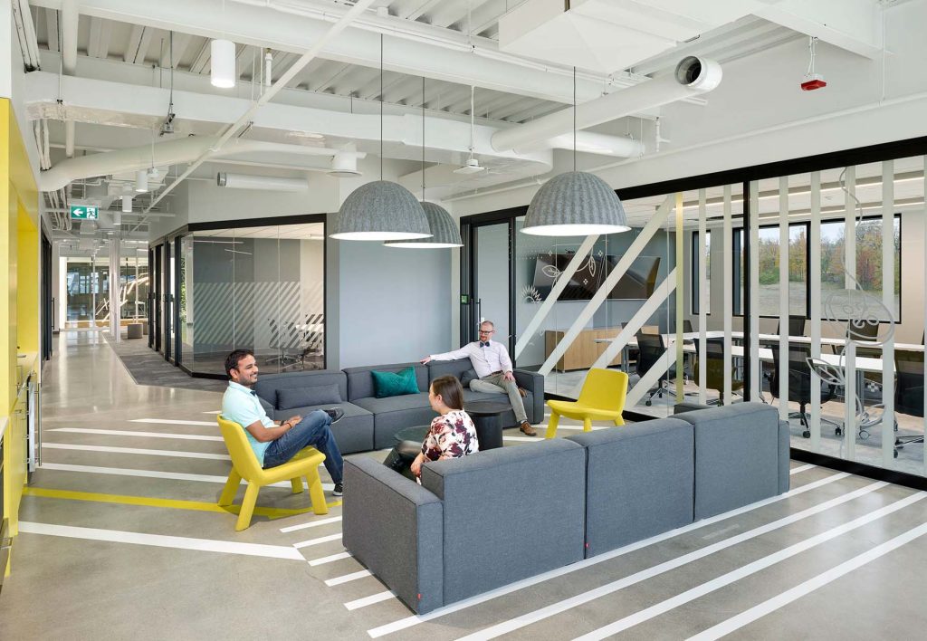 A seating area with two gray couches provides a casual space to connect, interspersed with punches of yellow for bright colour.