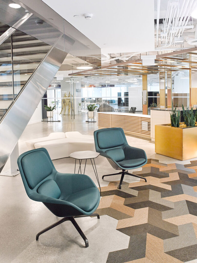 Teal colored lounge chairs on geometric patterned carpeting in a central lounging area of the office space