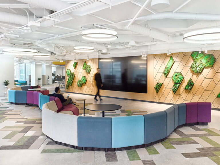 Curved multi coloured seating across from a large wooden wall housing a large screen and some vertical biophilic design elements on the wall
