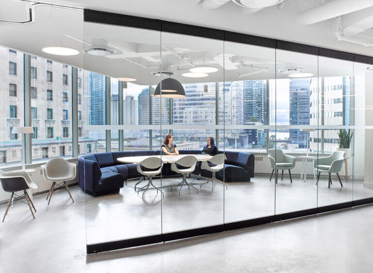 A casual meeting area surrounded by city views all around. A desk with a curved sofa on one side and chairs on the other.