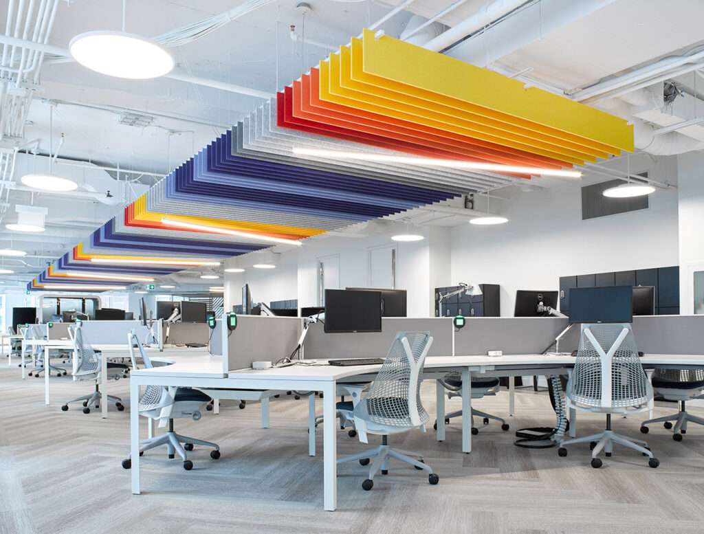Open concept, well lit and bright office space with modern work stations and colorful slats running along the ceiling above.