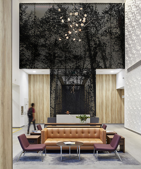 Lobby lounge area with back to back seating and the tall black metal screen behind it with the forest image imprinted on it. The elevator lobby visible through the black screen.