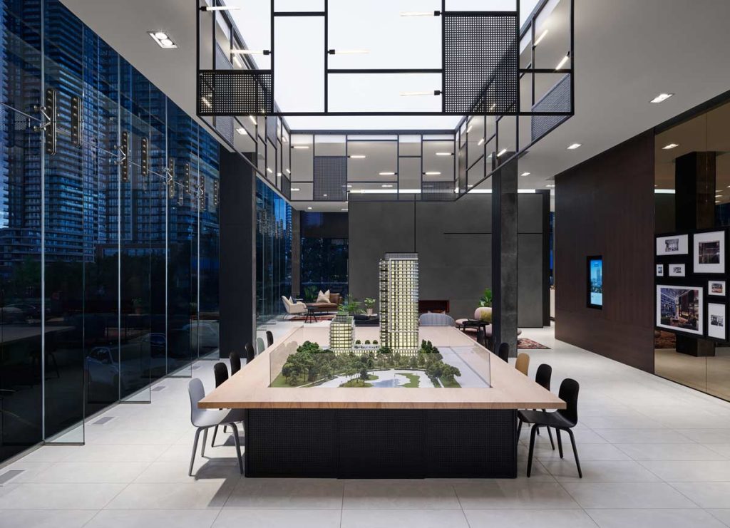 A large 3D model of the building displayed in a large space in the lobby area with metal details above, on the ceiling and wood a glass details on the wall displaying beautiful framed photographs of the property