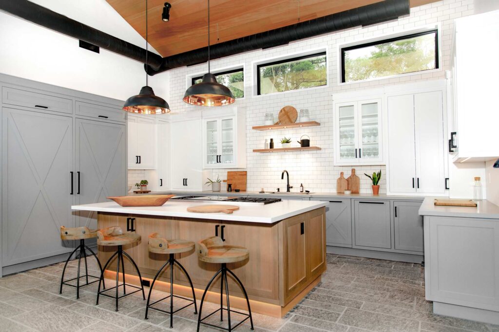 Predominantly white kitchen with grey lower cabinets and upper white cabinets, and a wooden island in the centre. There are industrial elements like the black metal windows, ceiling pipes and pendants above the island.