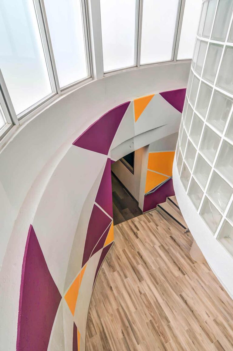 View from the gallery level down at the colorful feature wall in the ground level circulation area with a geometric design in deep purple and oranges