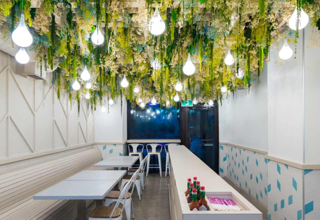 Dining area and the biophilic design hanging down from the ceiling with choreographed undulating light-droplets peeking through the greenery