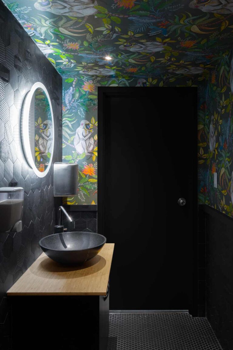 Washroom in dark monochromatic material finishes with a jungle themed wallpaper