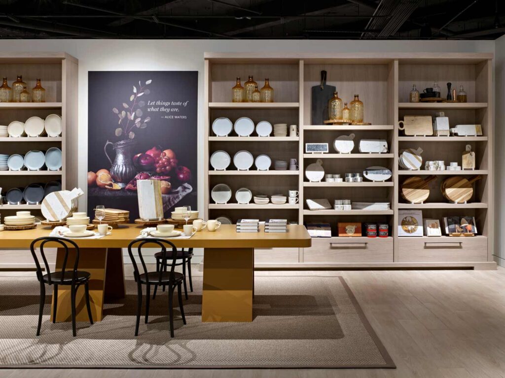 "Joy of the table" area, the section displaying homeware with floor to ceiling wall shelving and a stunning large dining table in front of them that showcases a table setting scene