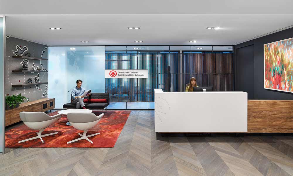 Contemporary reception area with warm accents wood finishes, red tones, a modern reception desk and waiting area with a large felt map of Canada across the entire wall