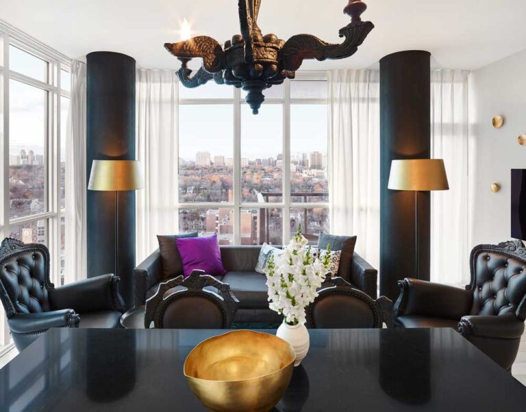 Living room showing black elegant furniture and gold accents on the wall and on the lamps, with night views of Toronto