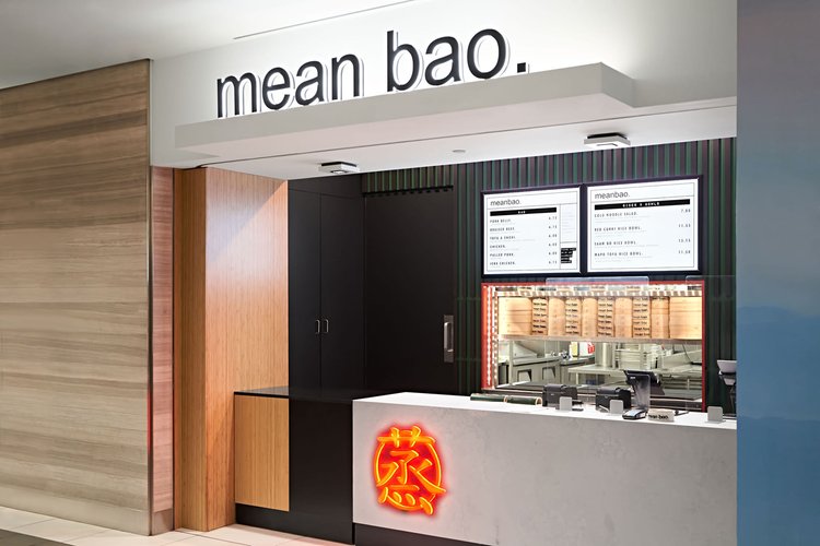 Side view of the Mean Bao fast food restaurant with whit concrete counter and red logo on it, and the slatted wall in the background