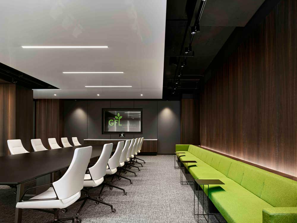 Meeting and conference room with long conference table at the endo of which is a large TV screen. Bench along the the length of the wall in an accent brand green color