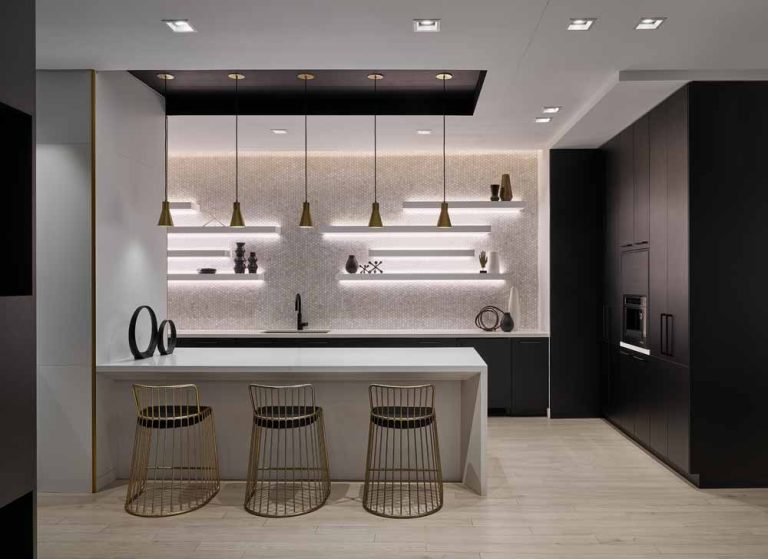 Black and white kitchen, white floating shelving on white mosaic tiled wall, with golden accents in lighting above the island and bar stools