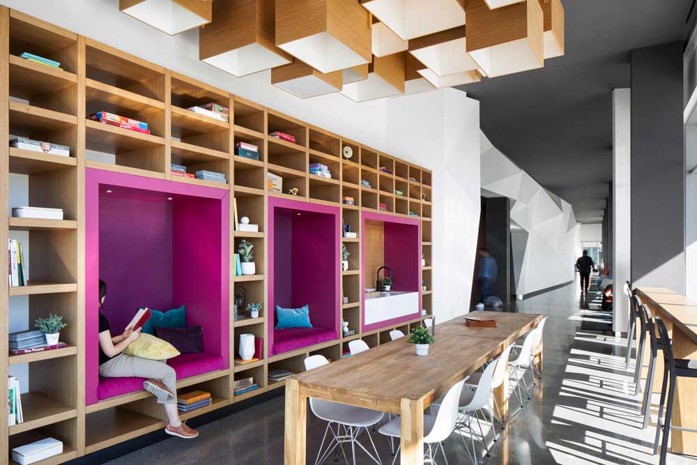 Another common area with encased in floor to ceiling windows and stunning wooden built in shelving unit on the wall with magenta accents to show built in seating