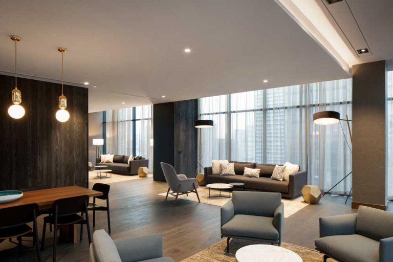 Lounge space on the top floor in a warm, sophisticated colour scheme and comfortable contemporary furniture overlooking the skyline through floor to ceiling windows all around