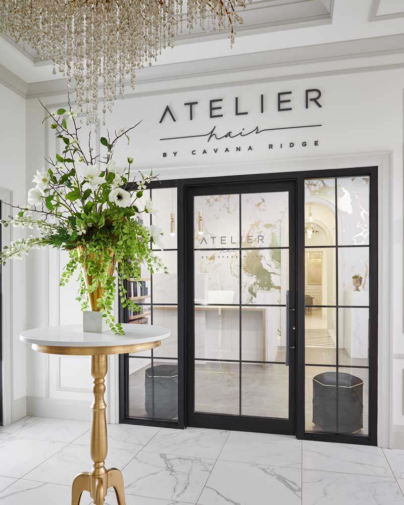 A view from the foyer to the main entrance to Atelier Hair that's salon visible through larhe glass door in blck framing