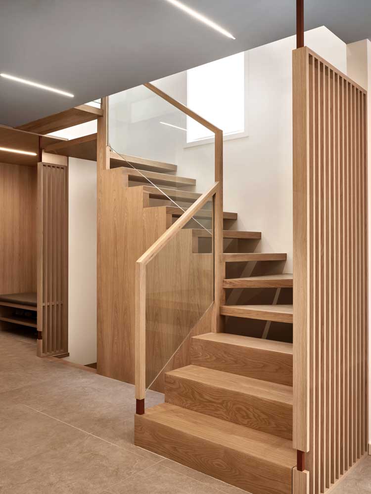 Stairs made of the same wood paneling material that is on the surrounding walls have some wooden slat details in place of railings on one side. On the other there are glass railings