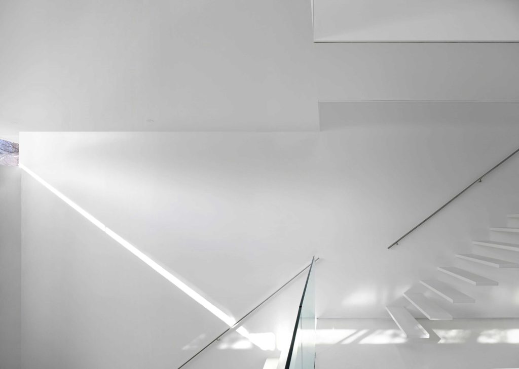 Light peeking through the narrow windows in the living area on the clean white walls nest to the stair case