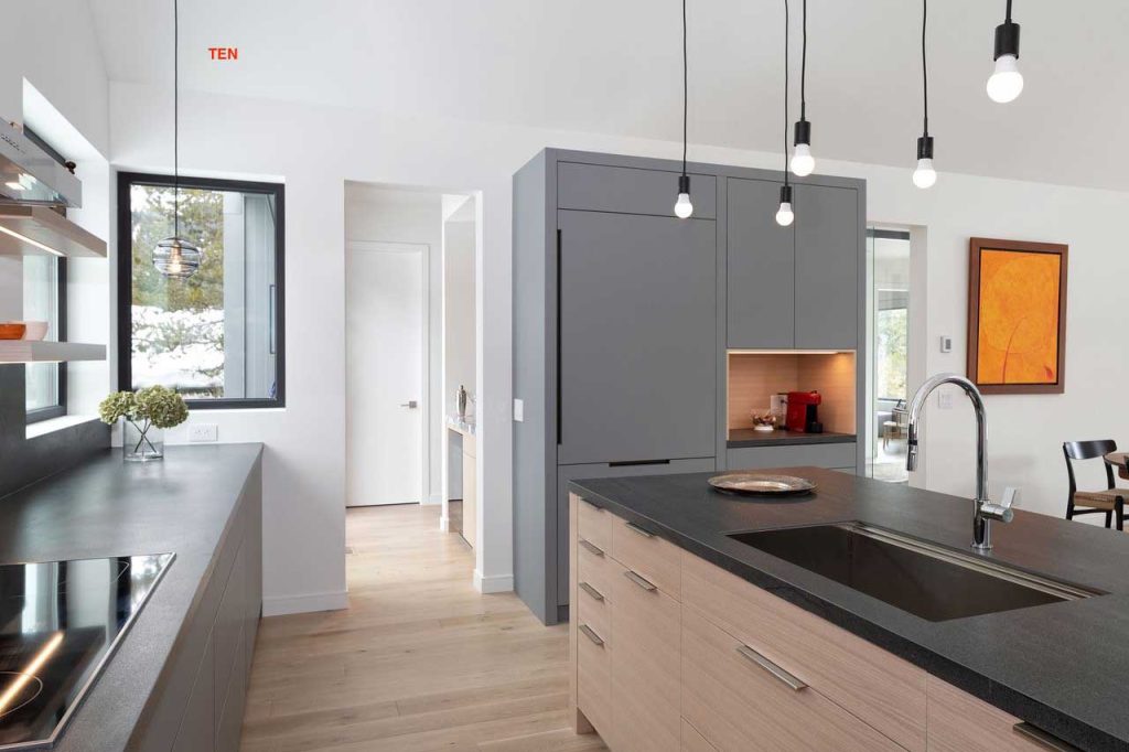 Minimalistic and modern kitchen in gray and wood tones and beautiful views out the window above the counter. A small wet bar is visible in the back room