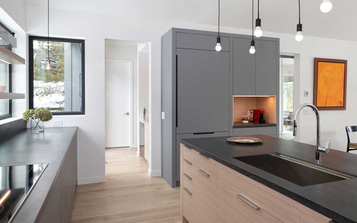 Minimalistic and modern kitchen in gray and wood tones and beautiful views out the window above the counter. A small wet bar is visible in the back room