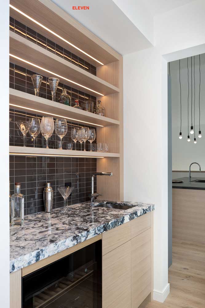 Wet bar just off the kitchen area done in light wood, dark wall tile behind the shelving and a bold-patterned countertop