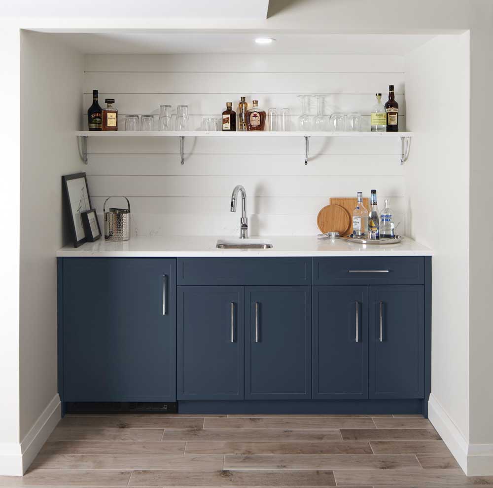 Wet bar in the basement with dark blue/gray bottom cabinets and white shiplap backsplash behind open shelving for drinks