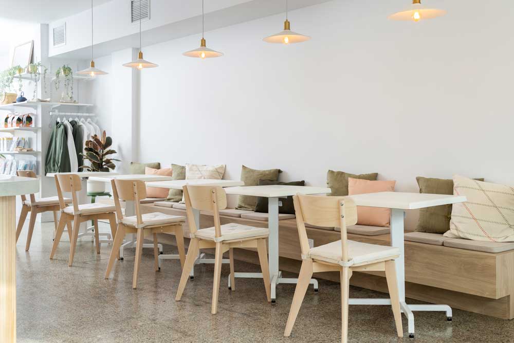 Simple seating area along the wall of the cafe as one walks in, with plain walls behind and simple white pendants. The comfy coushins bring in a calming colour palette